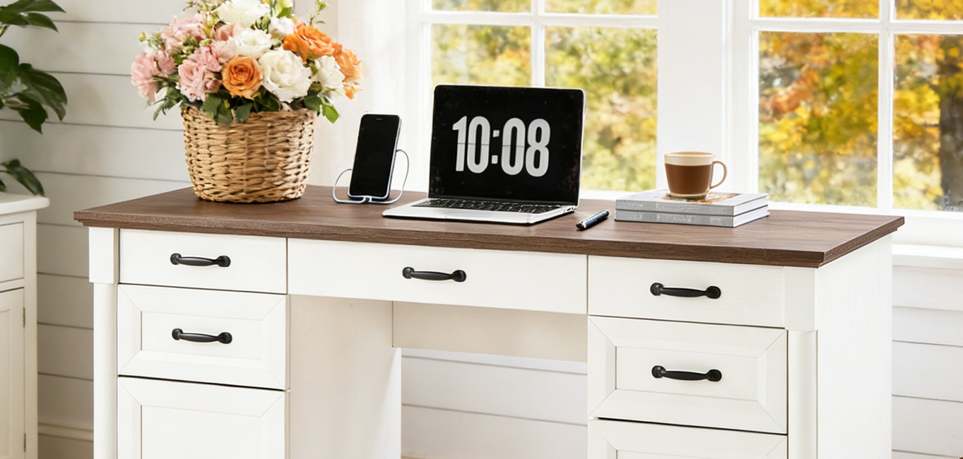 A white computer desk with drawers set against a window, styled with a laptop, a coffee cup and flowers.